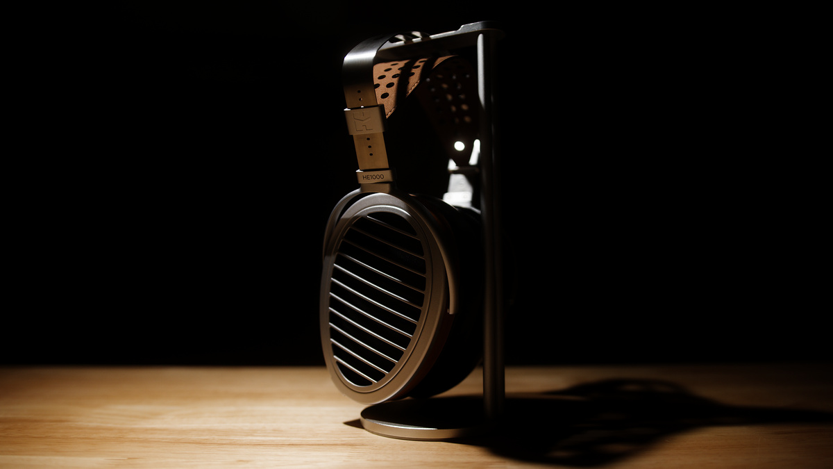 Open-back planar headphones on a stand over a wood surface, lit by a single hard light