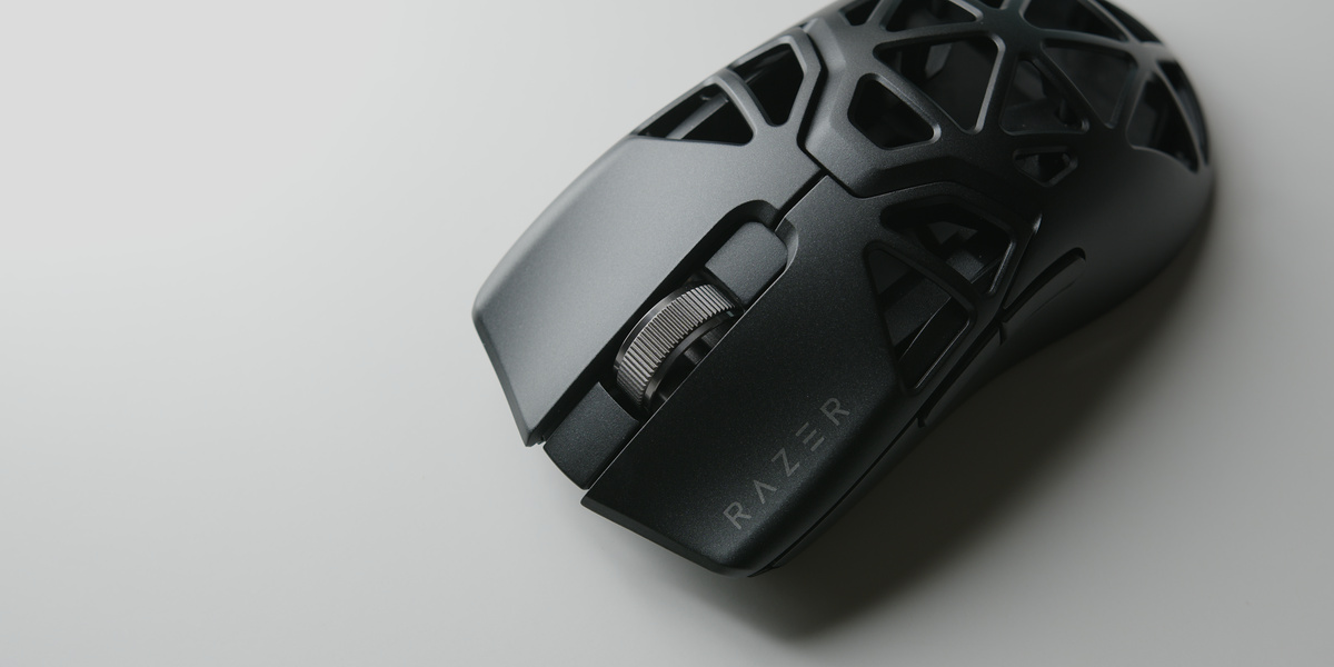 Dark open-frame gaming mouse on a light grey surface, showing shell texture and scroll wheel