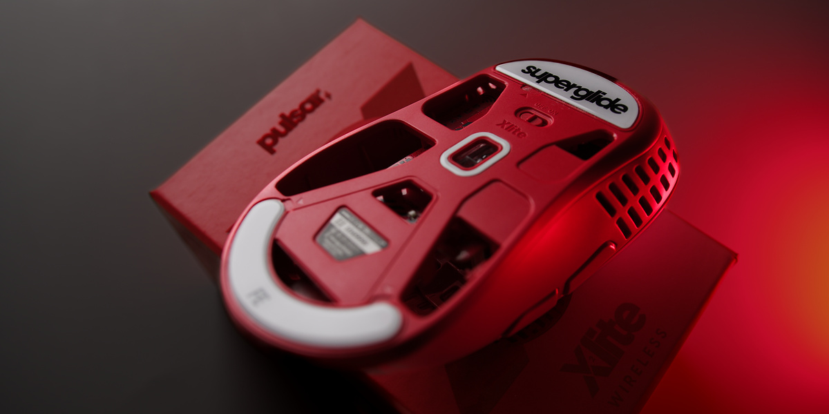 Underside of a red open-frame gaming mouse resting on its red box, in saturated red light