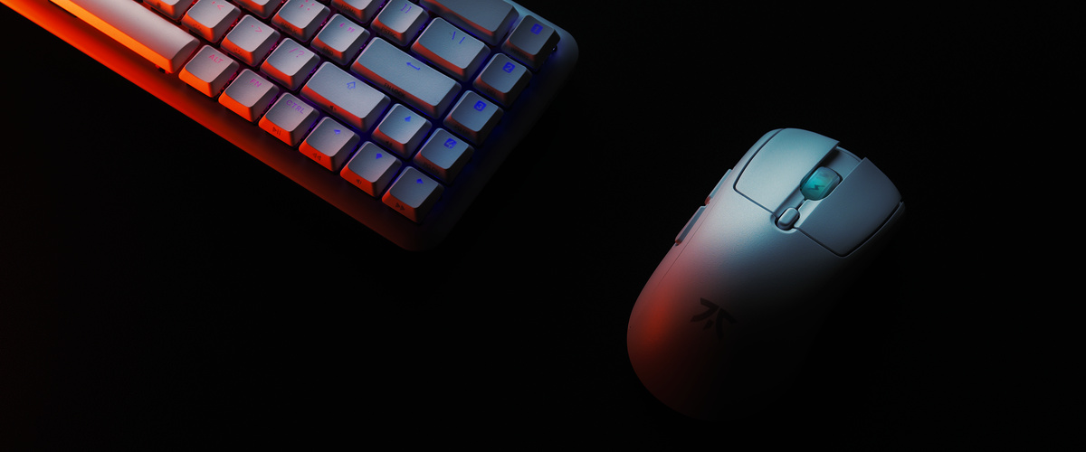 Compact keyboard and white gaming mouse on black, lit warm from one side and cool from the other
