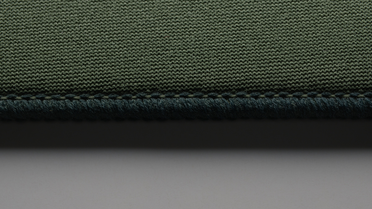 Macro of a dark green knit mousepad surface and stitched edge falling off into soft focus